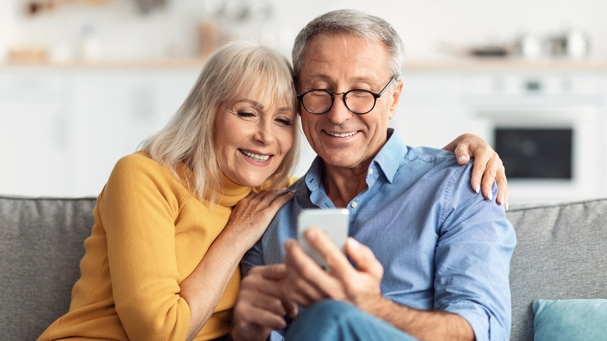 Couple souriant sur un canapé regardant un smartphone
